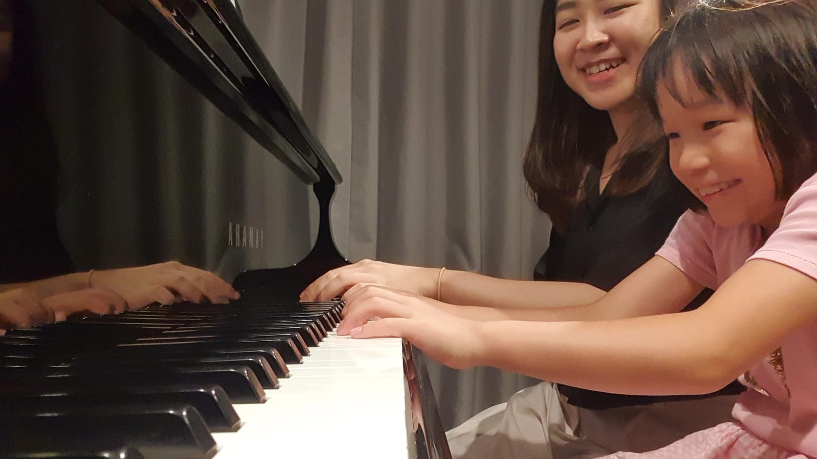Kathrine Leong and a young student laughing together at the keyboard during a lesson at home
