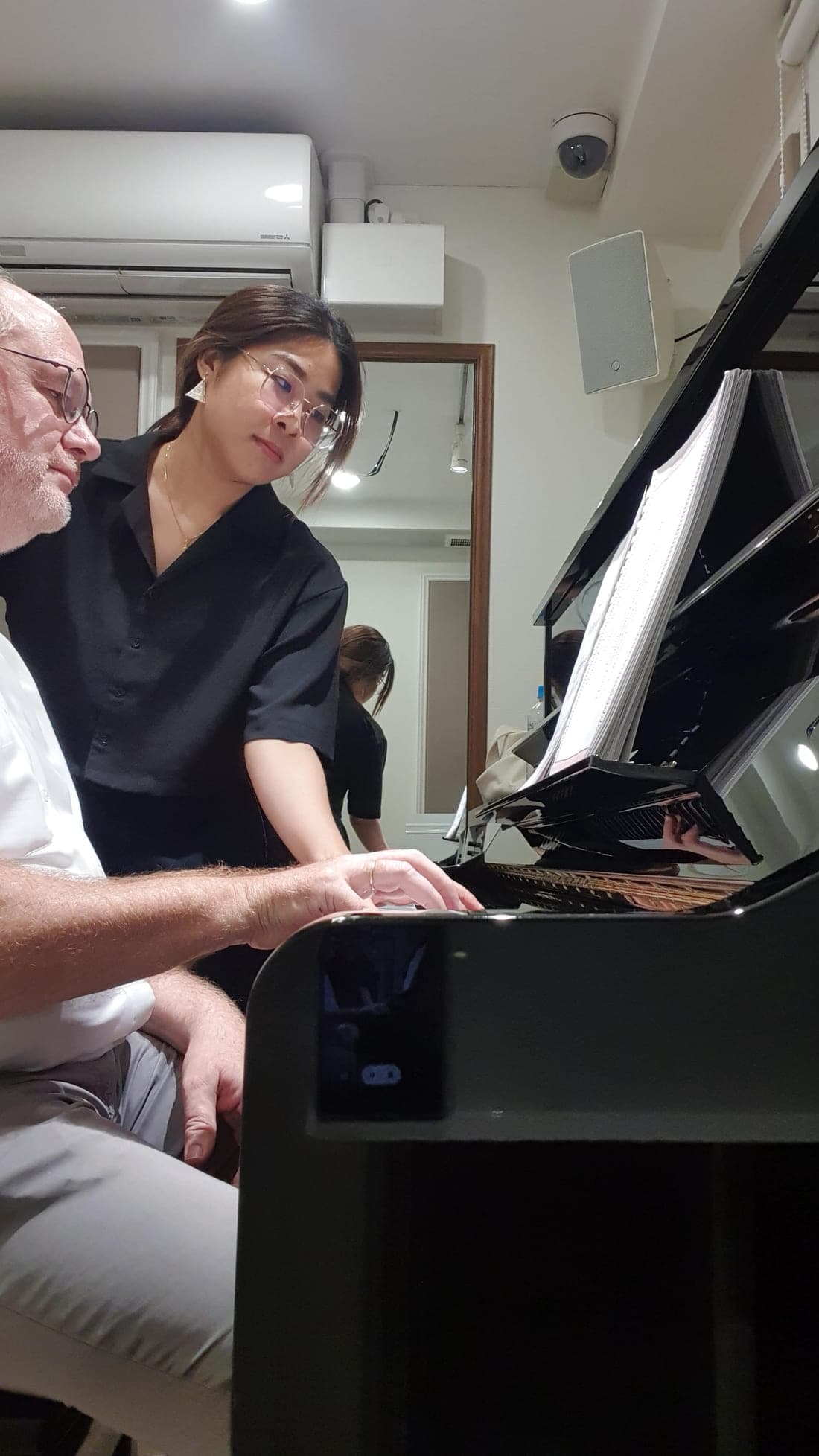 An adult student playing while Kathrine Leong follows the score in a music studio