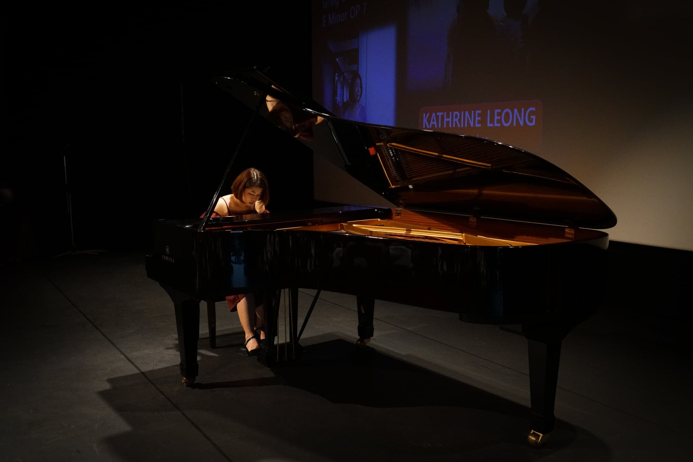 Kathrine Leong performing a solo piece at a concert grand under a stage spotlight