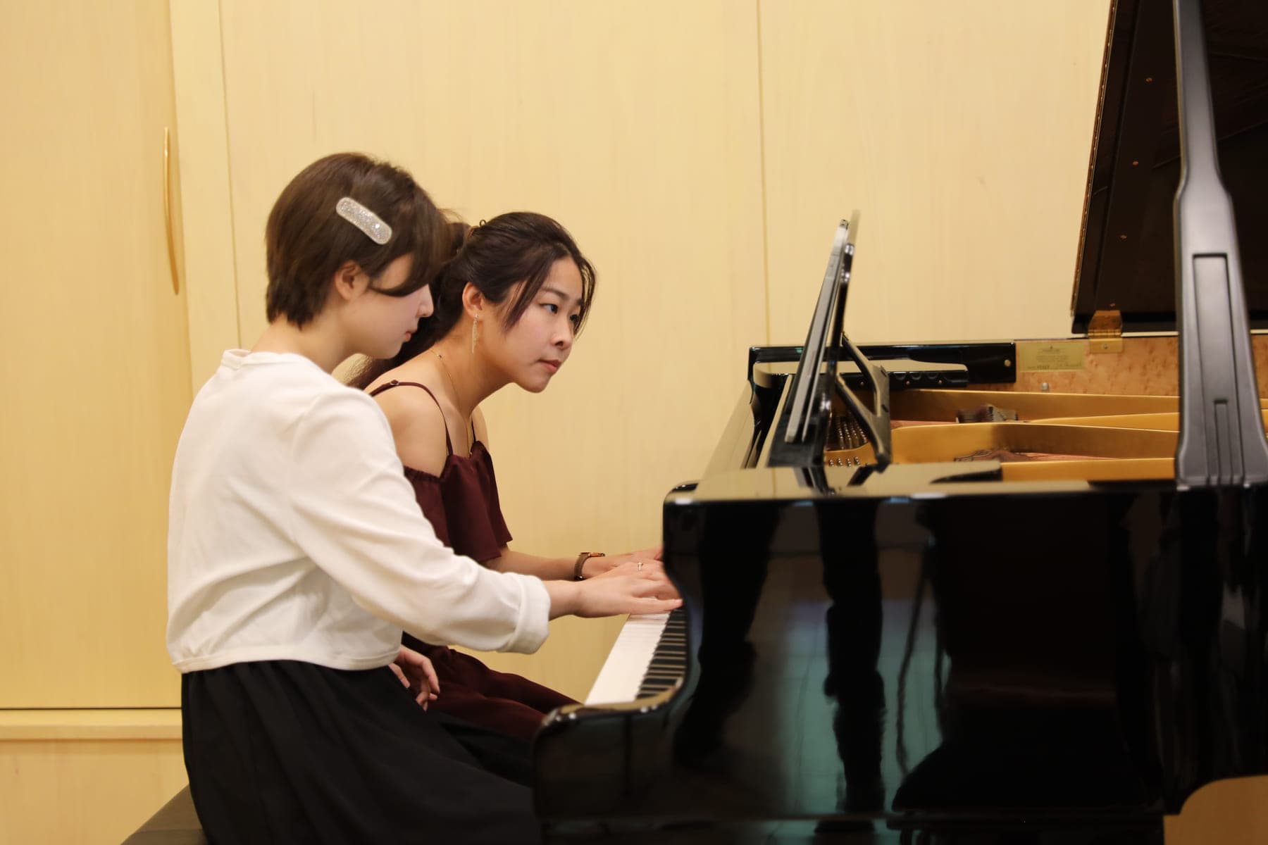 Two students playing a duet at the concert grand during a recital